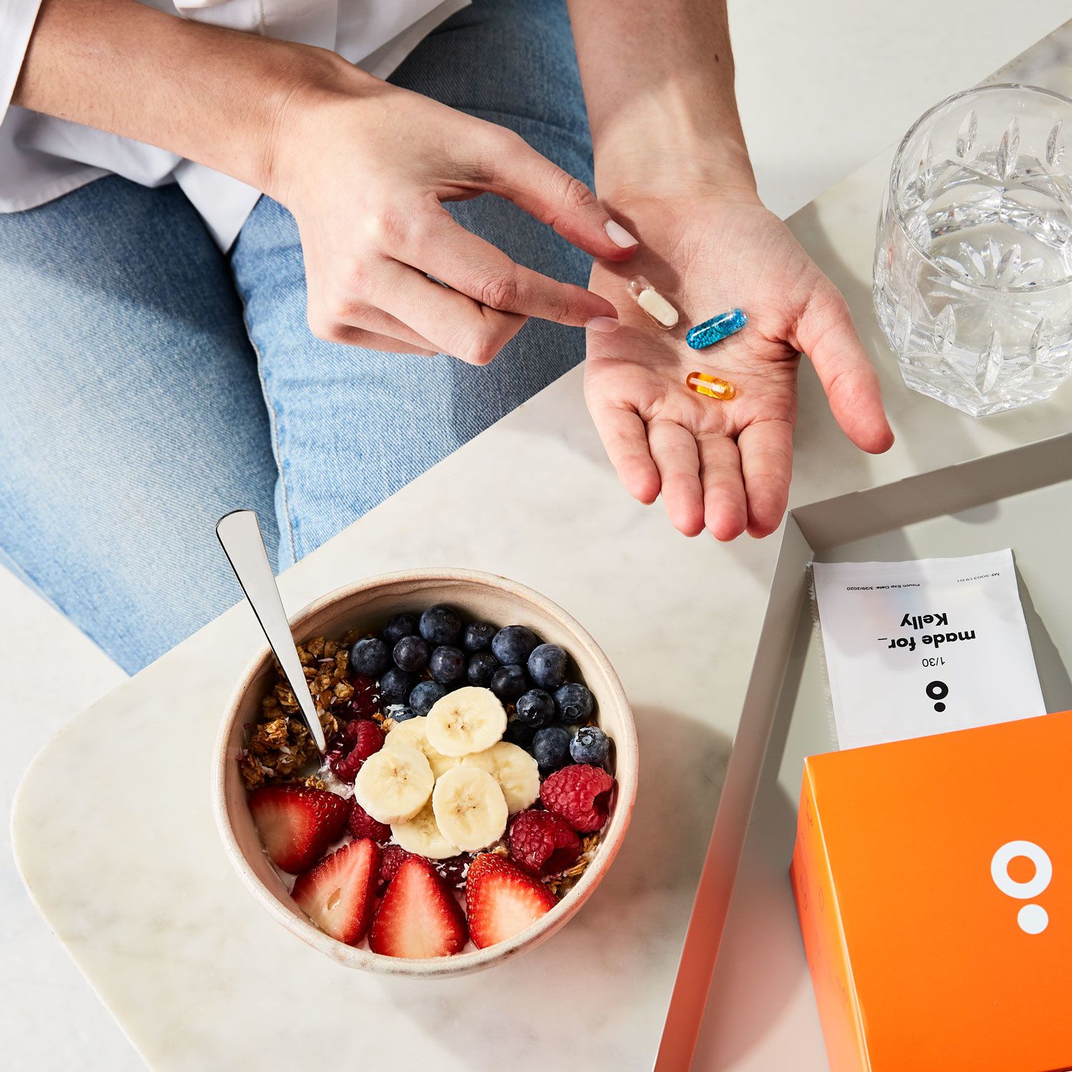 A woman holds a MadeFor_ pill while eating a breakfast bowl of fruits