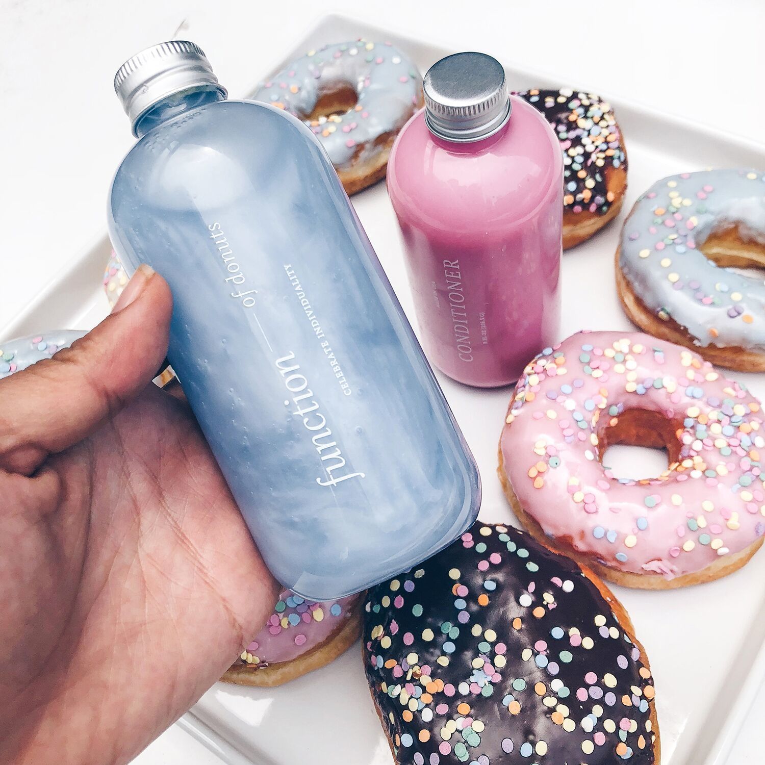 A hand holds a blue FOB haircare bottle in front of colorful donuts