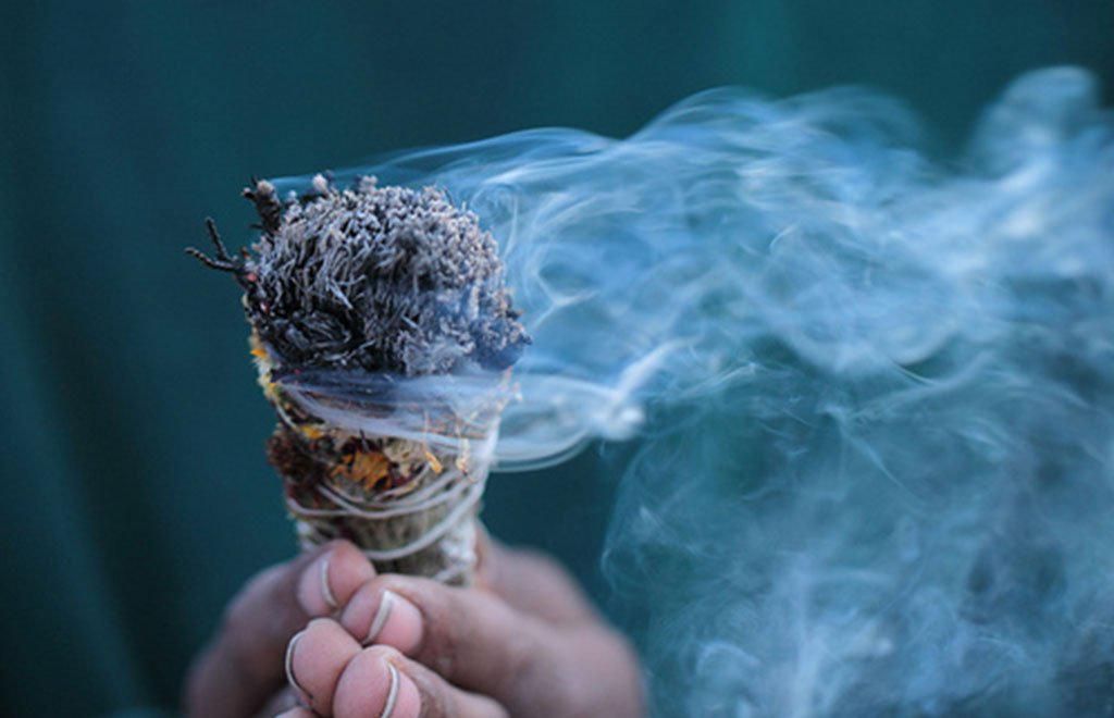 A bundle of white sage held between two hands with smoke pouring off of it