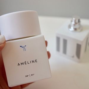 A thumb is visible holding a square white bottle that says AMELINE