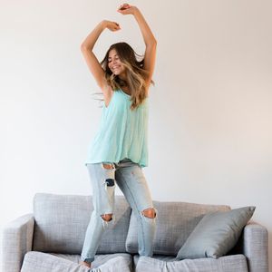 woman in jeans dances on a grey couch in a clean living room