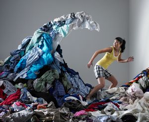 woman stands on a mountain of messy clothes, looks anxious