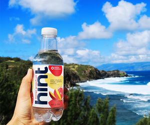 A bottle of hint mango-grapefruit water against beautiful blue skies and ocean waves