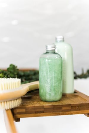 Two green bottles of Function of Beauty hair care next to a brush