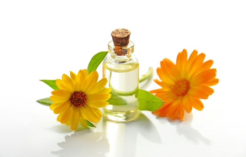 Small glass bottle of essential oil surrounded by flowers